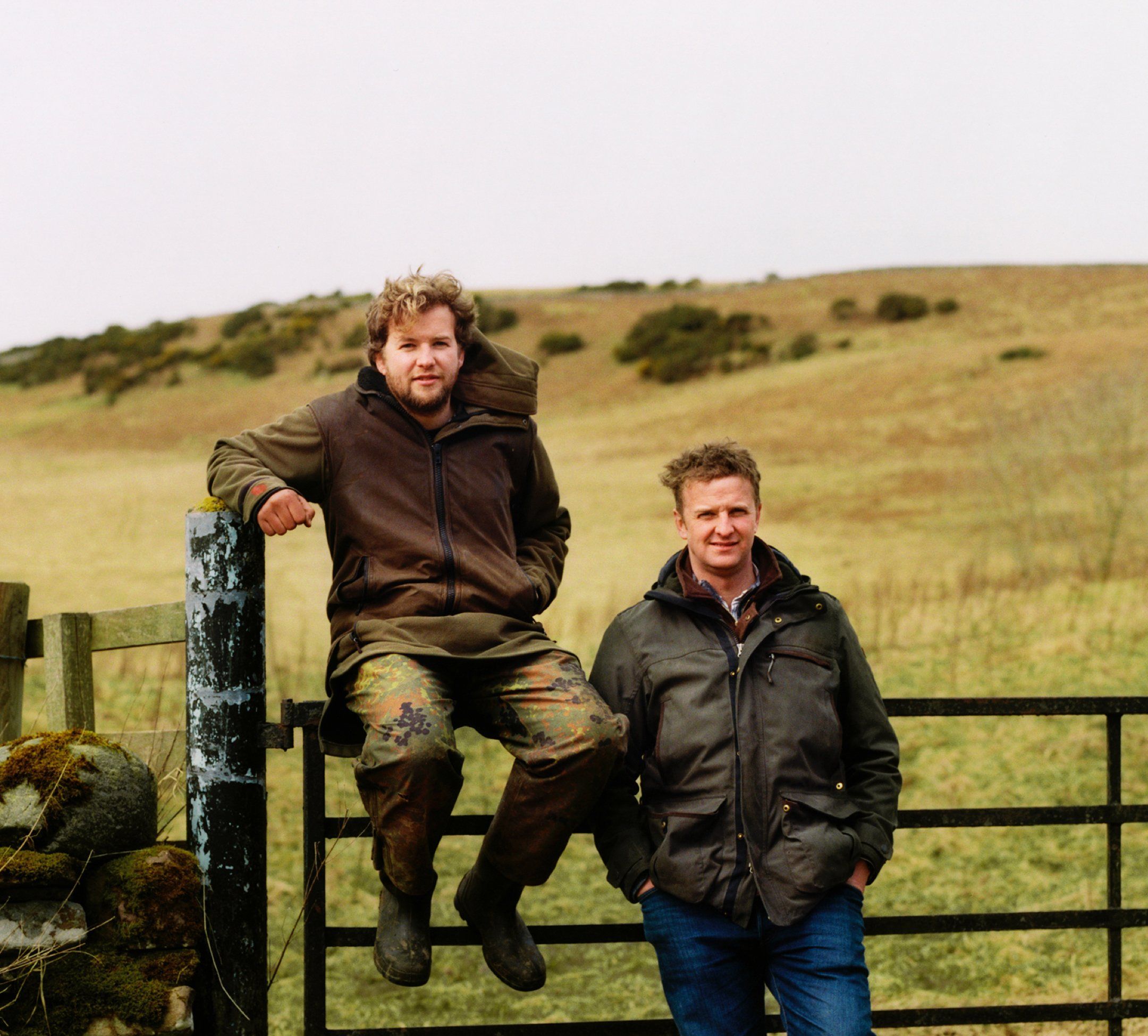 two farmers Andrew and Robert Brewster in work clothes sitting on a farm fence